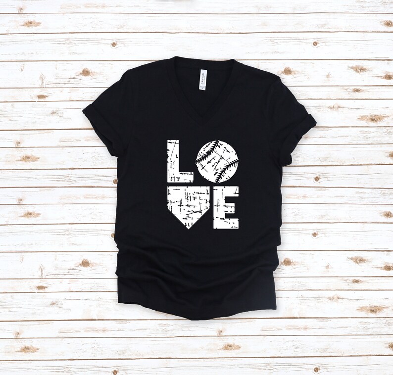 May include: Black V-neck t-shirt with a white graphic that says "LOVE" with a baseball replacing the "O". The baseball design has white stitching details. The shirt is made of a soft material.