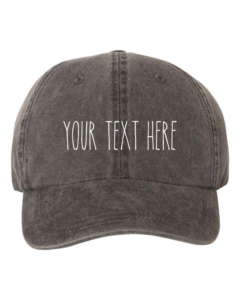 May include: A dark gray baseball cap with the text "YOUR TEXT HERE" in white. The cap has a curved brim and a classic six-panel design. The fabric appears to be a washed cotton or similar material.