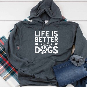May include: A dark gray hooded sweatshirt with the text "Life is better with DOGS" in white. The text is accompanied by a paw print and two arrows.