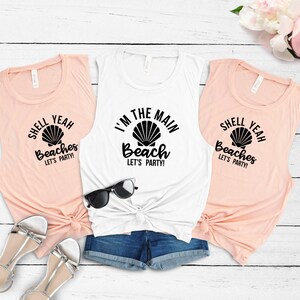 May include: Three sleeveless shirts with a beach theme. The white shirt says "I'm the Main Beach Let's Party!" with a seashell graphic. The two peach shirts say "Shell Yeah Beaches Let's Party!" with a seashell graphic.