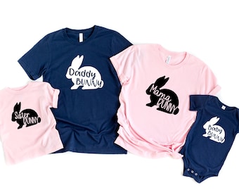May include: A set of four t-shirts featuring a bunny silhouette with the text "Daddy Bunny", "Mama Bunny", "Sister Bunny", and "Baby Bunny". The shirts are in navy blue and pink.