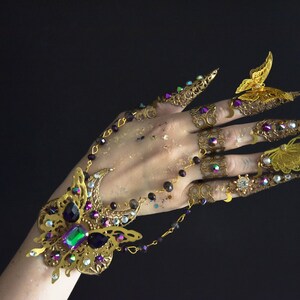 May include: A gold-toned butterfly-themed finger and wrist jewelry set. The set includes a bracelet with a large butterfly design and several rings with butterfly and claw designs. The jewelry is adorned with colorful gemstones.