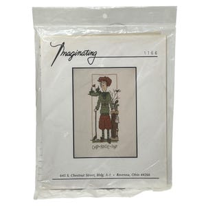 May include: A cross-stitch kit in a clear plastic package. The kit features a golf-themed design with a cartoon figure holding a golf club. The text "Imaginating" is at the top, and "CHIP-BIRDIE PAR" is at the bottom.