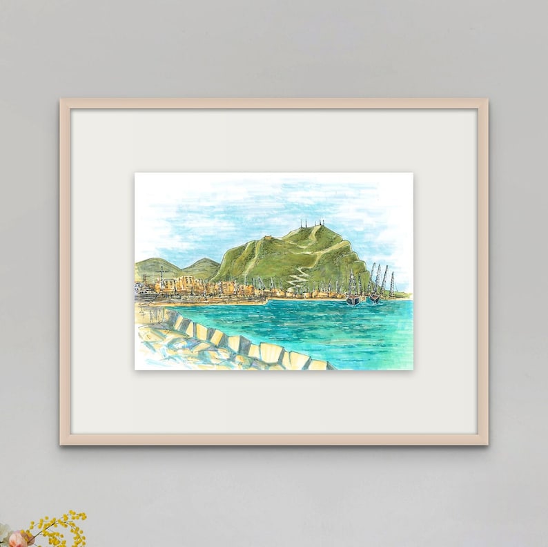 May include: A watercolor painting of a harbor scene with a green hill in the background. The water is a bright blue and there are several boats docked in the harbor. The painting is framed in a light wood frame.