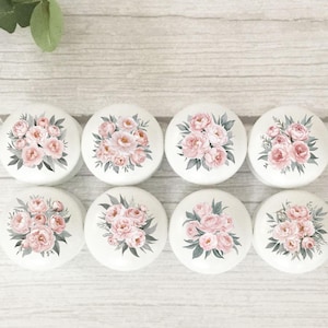 May include: Eight white ceramic knobs with pink and green floral designs. The knobs are arranged in two rows of four.