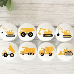 Op de afbeelding: Acht gele constructievoertuigknoppen met witte achtergronden. De voertuigen omvatten een ​​kipper, een betonmixer, een bulldozer, een kraan en een graafmachine.
