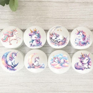 May include: Eight white round ceramic knobs featuring unicorn designs. The designs include a unicorn with a crown, a unicorn sleeping on a crescent moon, a unicorn standing on a flower, and a unicorn with a flower crown.
