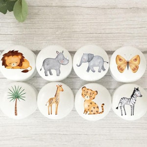 May include: Eight white round knobs with different animal and nature designs. The designs include a lion, rhino, elephant, butterfly, palm tree, giraffe, leopard, and zebra.