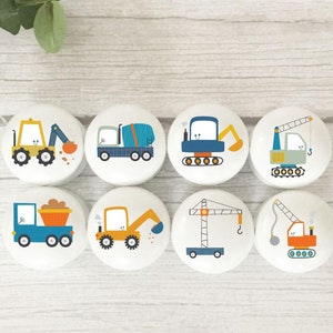 May include: Set of eight round wooden knobs featuring colourful construction vehicle designs. The designs include a cement mixer, excavator, crane, dumper truck, and bulldozer.