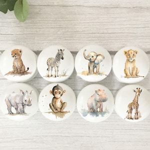 May include: Set of eight ceramic knobs featuring watercolour illustrations of various safari animals, including a cheetah, zebra, elephant, lion, rhinoceros, monkey, hippopotamus, and giraffe. The knobs are white with a light brown background.