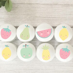 May include: Eight white cabinet knobs with cheerful fruit illustrations. The designs include a strawberry, pear, watermelon, lemon, apple, and pineapple, each with a smiling face. A fun and colourful design.