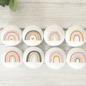May include: Eight round white ceramic knobs with rainbow designs. Each knob features a different colour combination of pink, blue, yellow, and grey with black polka dots. Some knobs have a small gold heart in the centre.