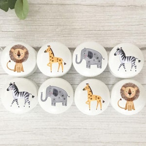 May include: Set of six white ceramic knobs featuring colourful animal illustrations. The animals include a lion, giraffe, elephant, zebra, and a second giraffe and lion.