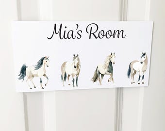 Puede incluir: Un letrero rectangular blanco con el texto negro Mia's Room centrado en la parte superior. Debajo del texto hay cuatro ilustraciones de caballos estilo acuarela en tonos blanco, crema y gris, cada uno en una pose diferente.