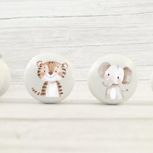 以下が含まれることがあります： 動物のイラストが描かれた白いセラミック製の引き出しノブが4つ。ノブには、ライオン、トラ、ゾウ、キリンが描かれています。