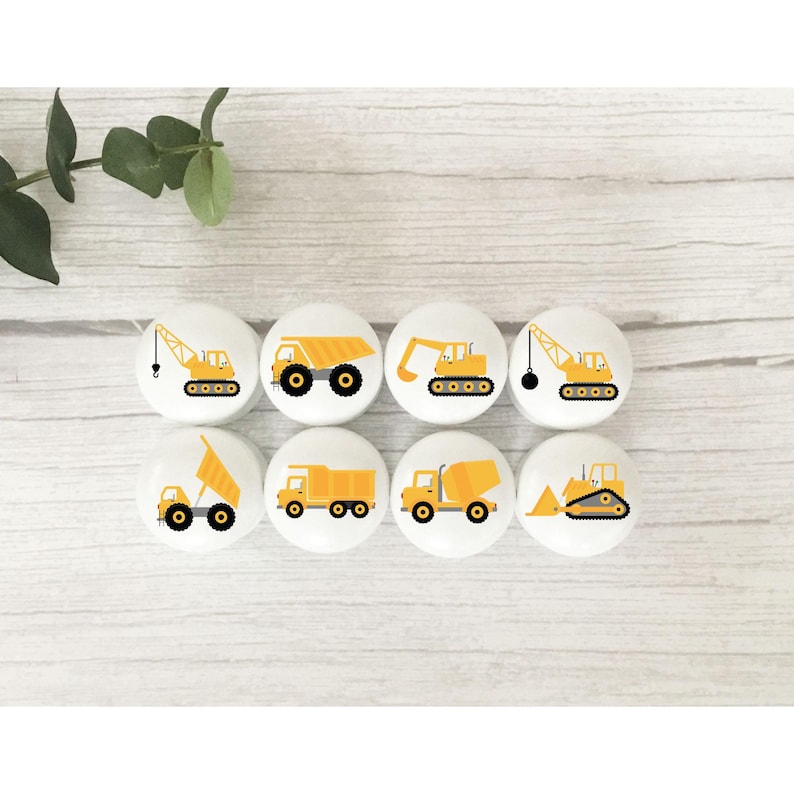 Op de afbeelding: Acht gele constructievoertuigknoppen met witte achtergronden. De voertuigen omvatten een ​​kipper, een betonmixer, een bulldozer, een kraan en een graafmachine.