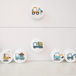 May include: Set of 7 white round drawer knobs with colourful construction vehicle designs. The knobs feature a cement mixer, a dumper truck, a crane, a bulldozer, and two excavators.