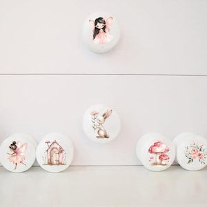 May include: Set of 7 white ceramic drawer knobs with various woodland creature and nature designs. The designs include a fairy, a rabbit, a mushroom, a birdhouse, a floral bouquet, and a deer.
