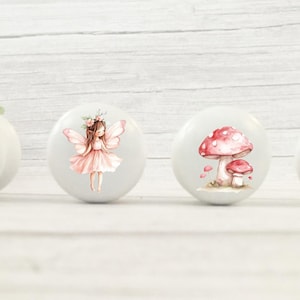 May include: Four white ceramic knobs with pink and brown woodland creature designs. The knobs feature a deer with a floral crown, a fairy with wings, a mushroom, and a butterfly.