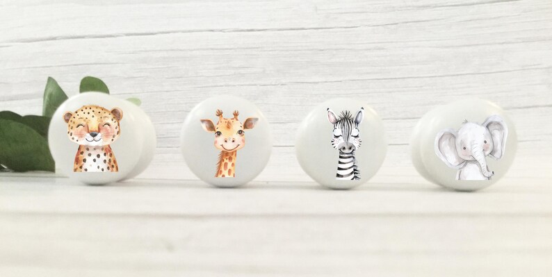 May include: Four white ceramic drawer knobs with animal illustrations. The knobs feature a cheetah, giraffe, zebra, and elephant.
