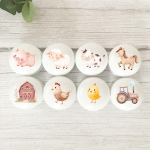 May include: Eight white ceramic cabinet knobs featuring farm animal illustrations. The knobs depict a pig, sheep, cow, horse, barn, chicken, chick, and tractor. The knobs are round with a glossy finish.