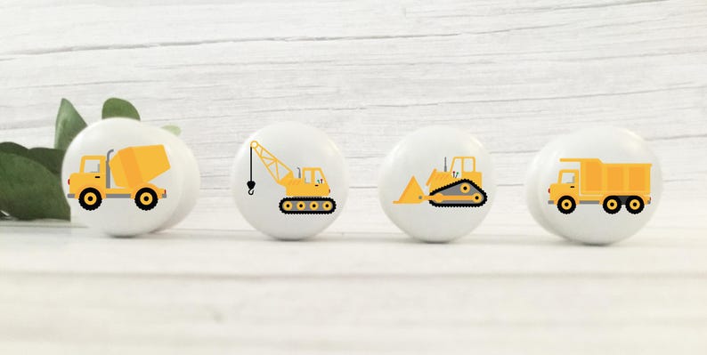 Op de afbeelding: Vier witte keramische knoppen met gele bouwvoertuigontwerpen. De knoppen tonen een betonmixer, een kraan, een bulldozer en een kiepwagen.