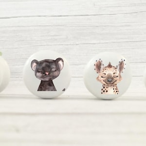 May include: Four white ceramic knobs with animal illustrations. The knobs feature a flamingo, a black panther, a hyena, and a gazelle.