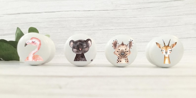 May include: Four white ceramic knobs with animal illustrations. The knobs feature a flamingo, a black panther, a hyena, and a gazelle.