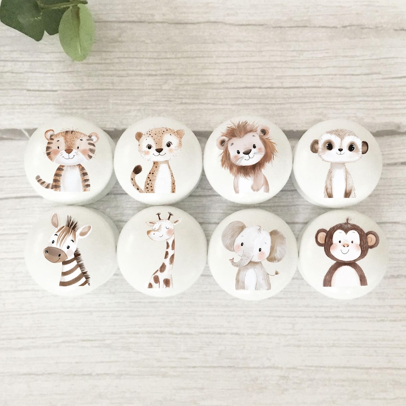 May include: Set of eight white round knobs with different animal illustrations. The animals include a tiger, cheetah, lion, meerkat, zebra, giraffe, elephant, and monkey.