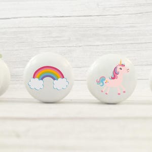 May include: Four white cabinet knobs with colourful designs. One knob features a pink castle, another a rainbow, and the other two show pink unicorns. Ideal for a child's bedroom or nursery.