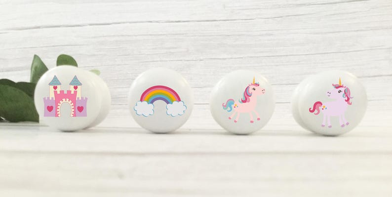 May include: Four white cabinet knobs with colourful designs. One knob features a pink castle, another a rainbow, and the other two show pink unicorns. Ideal for a child's bedroom or nursery.