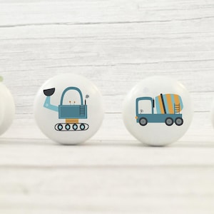 May include: Four ceramic knobs featuring different construction vehicle designs. The knobs are white with blue, yellow and orange accents. The vehicles include a cement mixer, a backhoe, a bulldozer and a dumper truck.