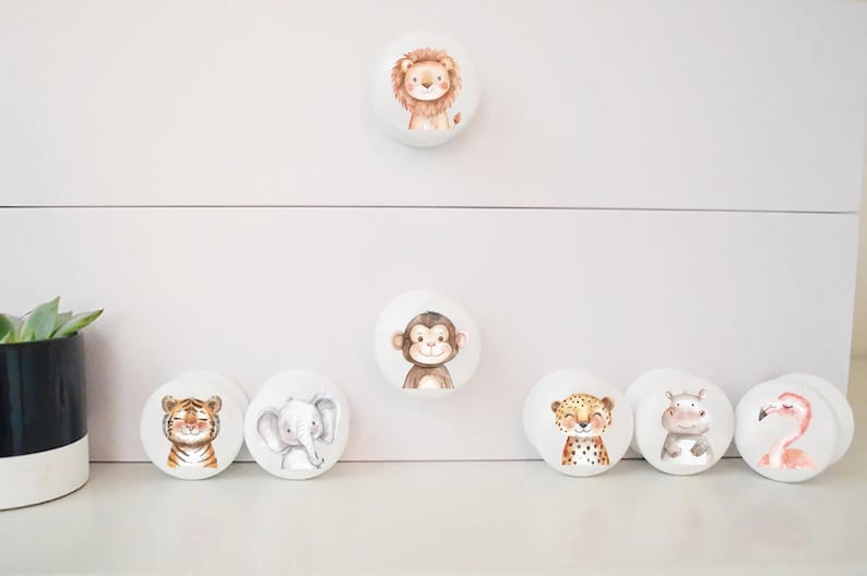 May include: Set of 7 white round drawer knobs with different animal illustrations. The animals include a lion, monkey, tiger, elephant, cheetah, hippopotamus, and flamingo.
