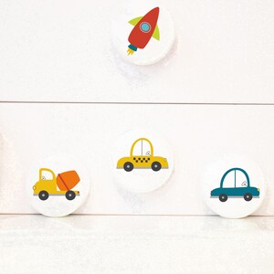 May include: Four round white stickers with colourful illustrations of a rocket, a yellow car, a blue car, and a yellow cement truck.