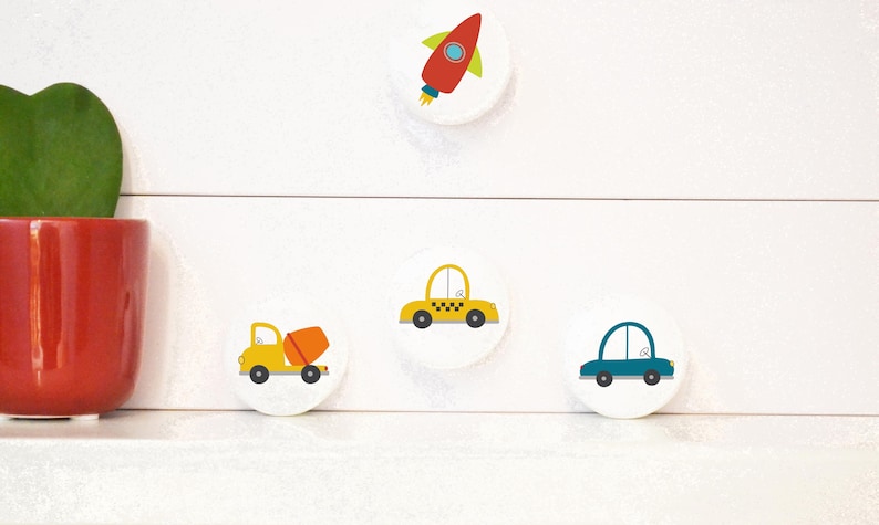 May include: Four round white stickers with colourful illustrations of a rocket, a yellow car, a blue car, and a yellow cement truck.