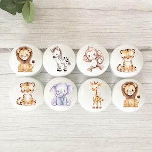 May include: Eight white ceramic cabinet knobs, each decorated with a different animal illustration. The collection includes a lion, zebra, monkey, tiger, elephant, and giraffe. The knobs are in soft colours, suitable for a nursery or children's bedroom.