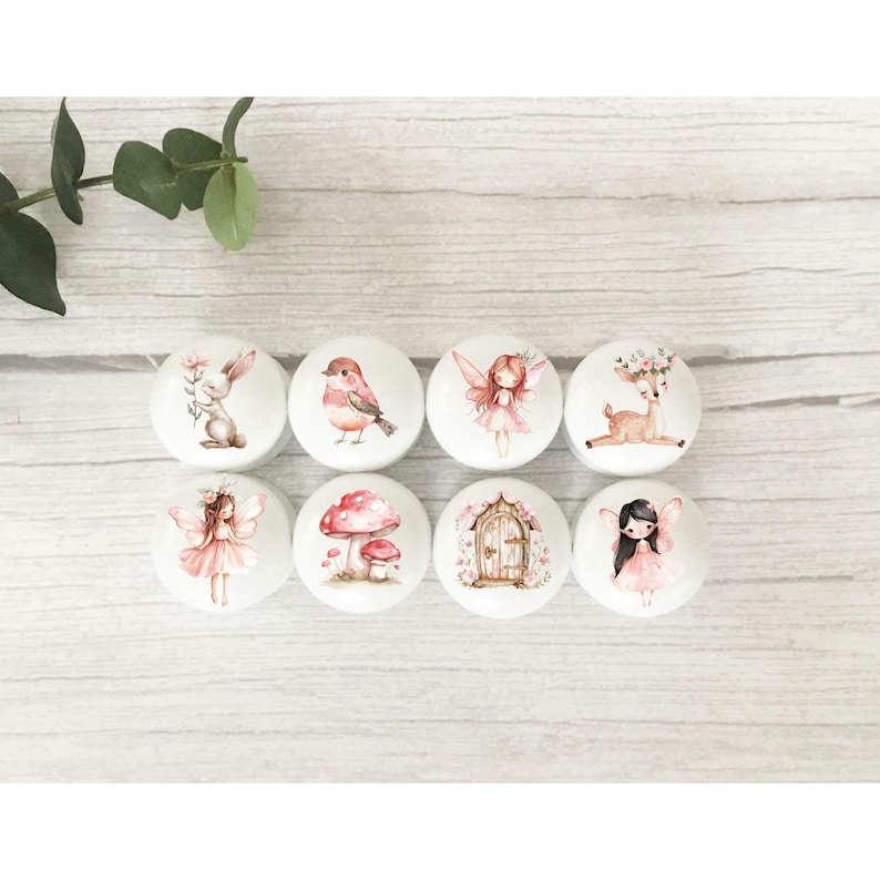 May include: Eight round white ceramic knobs with various woodland creature and fairy designs. The designs include a rabbit, bird, fairy, deer, mushroom, door, and two fairies.