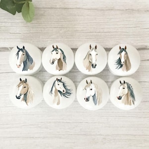 May include: A set of eight round white cabinet knobs, each featuring a unique watercolour illustration of a horse head. The horses are depicted in various shades of brown, grey, and white, showcasing different mane styles and facial markings.