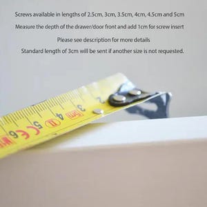 K&ouml;nnte beinhalten: Ein gelbes Ma&szlig;band mit schwarzen Markierungen wird verwendet, um die Tiefe einer wei&szlig;en Schubladenfront zu messen. Das Ma&szlig;band zeigt 3 cm, 4 cm und 5 cm an. Der Text auf dem Bild lautet: "Schrauben in L&auml;ngen von 2,5 cm, 3 cm, 3,5 cm, 4 cm, 4,5 cm und 5 cm verf&uuml;gbar. Messen Sie die Tiefe der Schubladen-/T&uuml;rfront und addieren Sie 1 cm f&uuml;r die Schraubeneins&auml;tze. Weitere Details finden Sie in der Beschreibung. Die Standardl&auml;nge von 3 cm wird versandt, wenn keine andere Gr&ouml;&szlig;e angefordert wird."