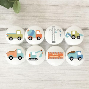 May include: Eight white cabinet knobs with colourful construction vehicle designs. The knobs feature images of a truck, cement mixer, crane, excavator, dump truck, and a sign that says "UNDER CONSTRUCTION".
