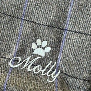 May include: A brown and white plaid dog blanket with a white paw print and the name "Molly" embroidered on it.