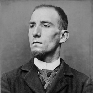 May include: Black and white portrait photograph of a man wearing a dark suit and a patterned tie. The photo is labelled with the number -217. 662.