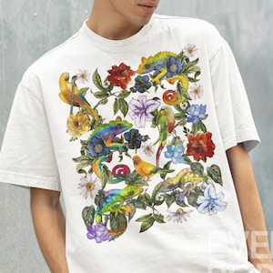 May include: White t-shirt with a colorful print of parrots and chameleons on a floral background. The print features green, blue, yellow, red, and orange colors.