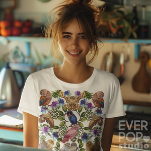 May include: White t-shirt featuring a colorful owl and floral design. The graphic includes various owls, blue and purple flowers, and green leaves. The text "EVER POP studio" is printed on the lower right side of the shirt.