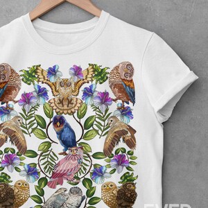 May include: White t-shirt featuring a colorful owl and floral design. The design includes various owls, blue and purple flowers, and green leaves. The shirt is displayed on a wooden hanger against a gray background. The text "EVER POP studio" is visible.