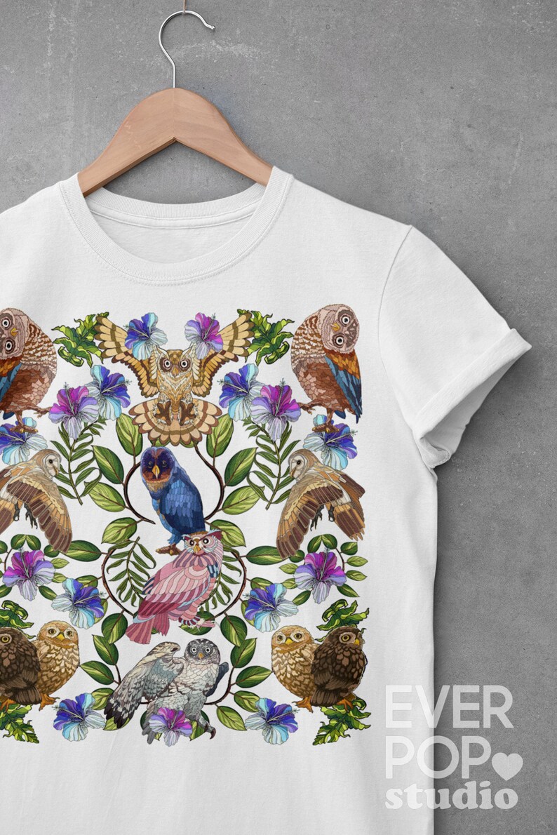 May include: White t-shirt featuring a colorful owl and floral design. The design includes various owls, blue and purple flowers, and green leaves. The shirt is displayed on a wooden hanger against a gray background. The text "EVER POP studio" is visible.