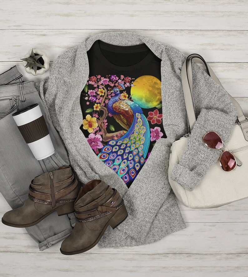May include: Black t-shirt with a colorful peacock design on a branch with pink flowers. The peacock has blue, green, and gold feathers. There is a yellow sun behind the peacock.