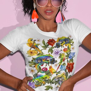 May include: White t-shirt with a colorful floral print featuring parrots, lizards, and flowers. The print is a vibrant mix of green, yellow, blue, red, and orange.