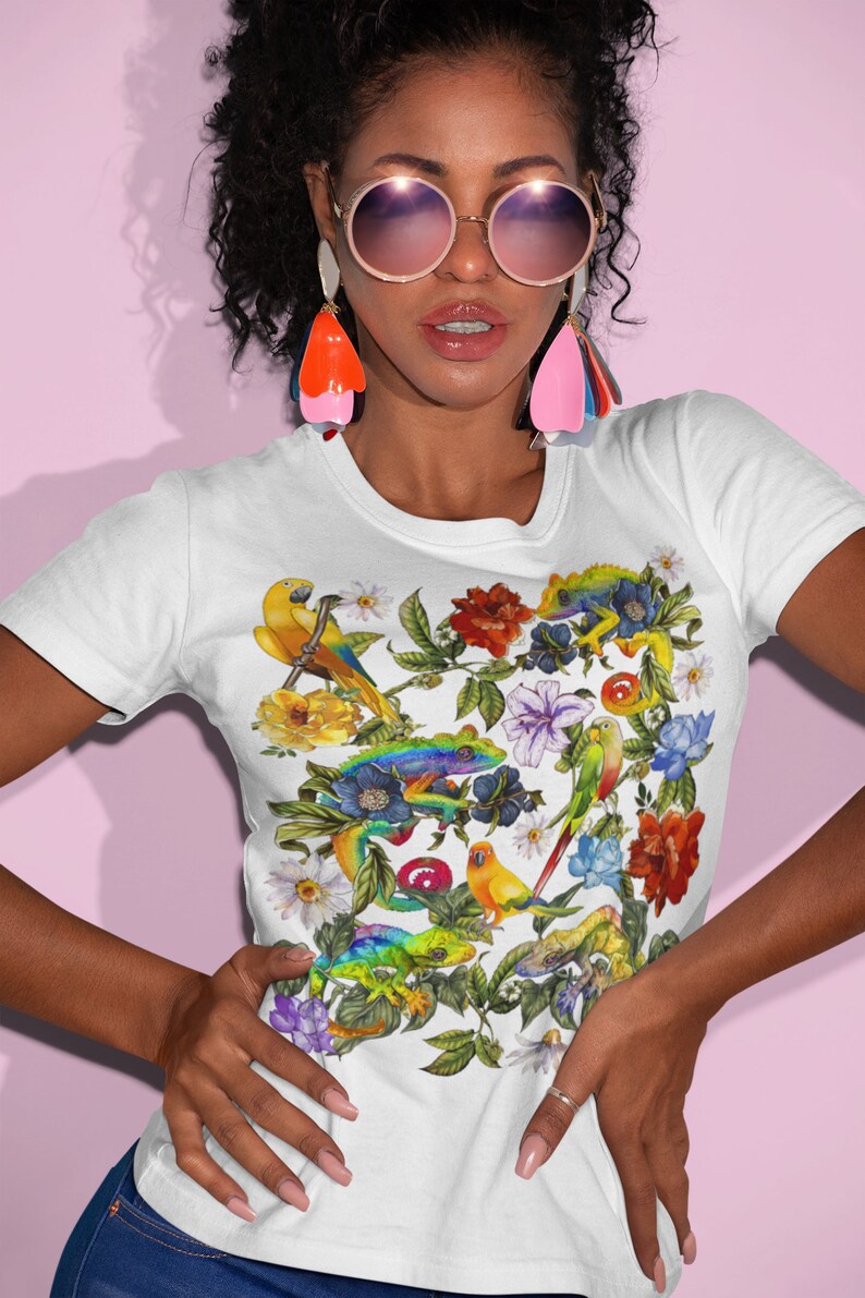 May include: White t-shirt with a colorful floral print featuring parrots, lizards, and flowers. The print is a vibrant mix of green, yellow, blue, red, and orange.