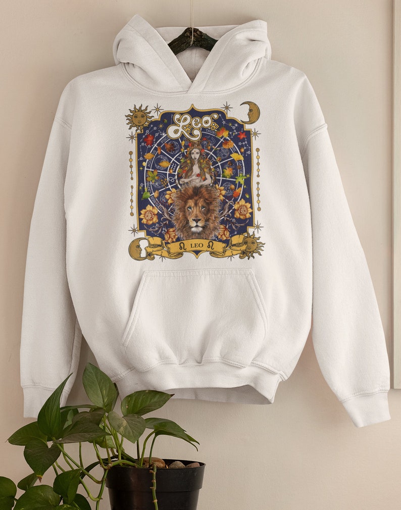 May include: White hoodie with a graphic print of a lion and a woman with a crown of leaves. The graphic is surrounded by stars, moons, and a zodiac wheel. The text "Leo" and "&Omega; LEO &Omega;" is printed on the graphic.